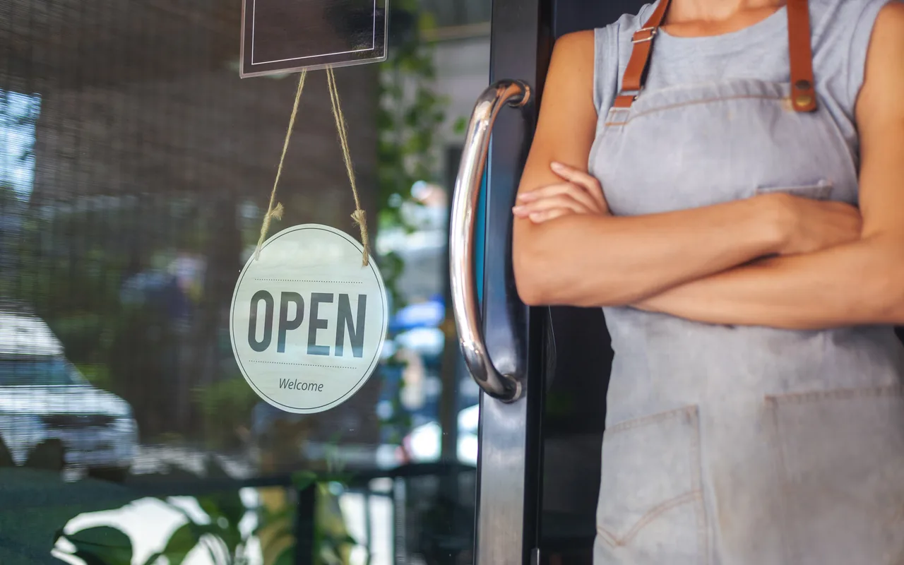 A small-business owner standing in their shop by an open sign
